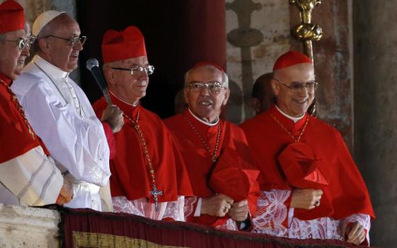Pope Francis, wearing papal white, stands among four cardinals wearing birettas and zucchettos on a balcony