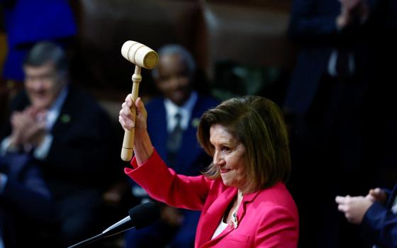 Nancy Pelosi, wearing a bright pink blazer, lifts a gavel high in the air