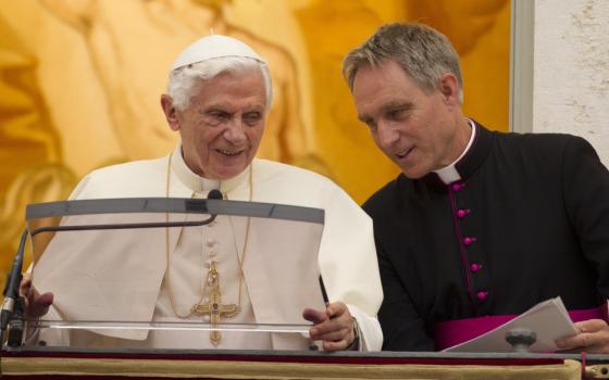 A white archbishop stands beside and leans toward Pope Benedict XVI
