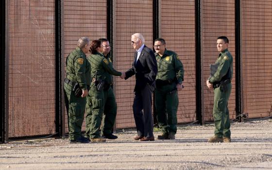 Biden, wearing a suit and aviators, shakes a Border Patrol agents hand by the border fence