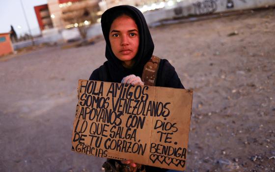 Yalimar Chirinos, a 19-year-old migrant from Venezuela, displays a sign near the U.S.-Mexico border in Ciudad Juárez, Mexico, Jan. 7. The sign reads, "Hello friends, we are from Venezuela, support us with what comes out from your heart. Thank you. God bless you." (OSV News/Reuters/Jose Luis Gonzalez)