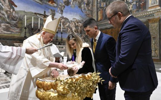 Pope Francis wears a mitre and baptizes a baby over a gold baptismal font as parents stand by
