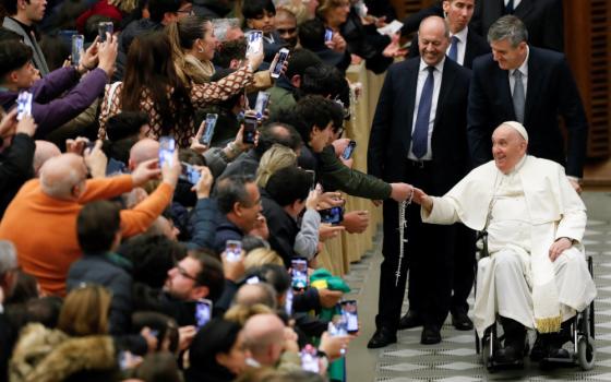 Pope Francis, with a big smile, wheels past an excited audience where people hold their cellphones up