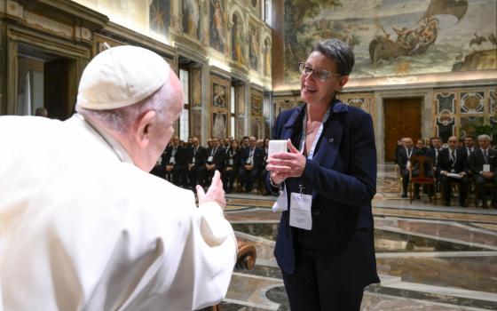 A white woman with short hair and glasses stands in front of Pope Francis with a large group behind her