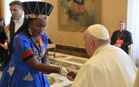 A Black woman wearing a colorful dress and a headdress shakes Pope Francis' hand