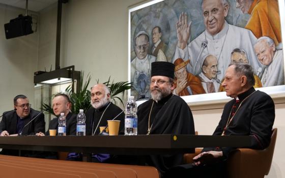 Five white men in black religious garb sit behind a long table with microphones