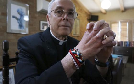 A white bishop wearing glasses and brightly colored friendship bracelets folds his hands