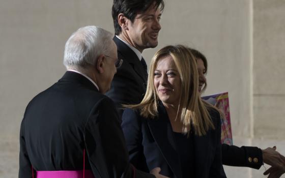 A white woman with honey blond hair shakes a cardinal's hand. Two people stand behind her.