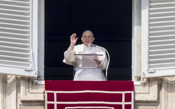 Pope Francis raises his hand as he stands behind a lectern in his window overlooking St. Peter's Square