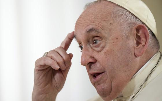 Pope Francis touches a finger to his forehead as he speaks