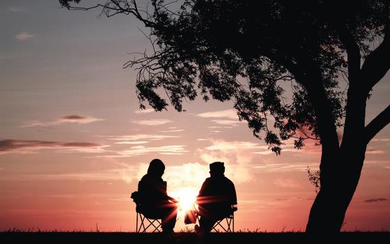 Two people seated outside, watching a sunset (Unsplash/Harli Marten)