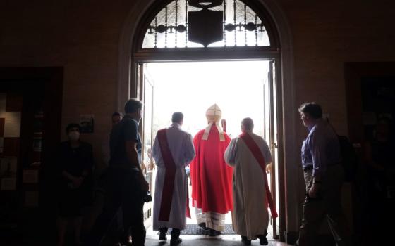 Cardinal is shown exiting a church, flanked by clergy. 