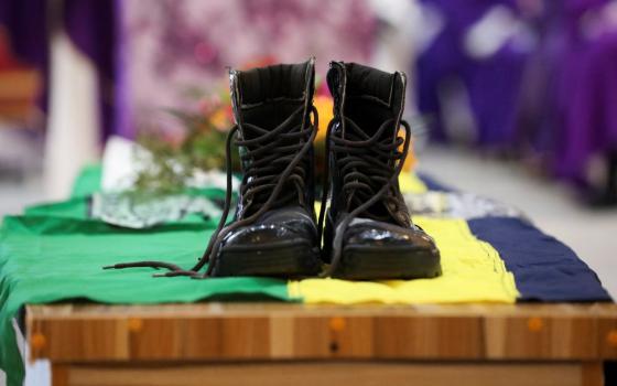Black work boots sit atop a Nigerian flag, which is draped over a coffin.