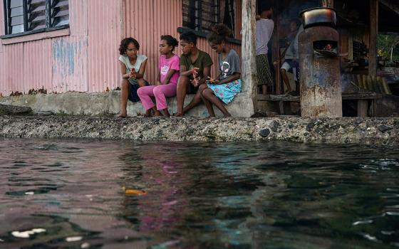 Village children pass the time in front of a home next to a flooding sea wall at high tide July 15, 2022, in Serua Village, Fiji. As the community runs out of ways to adapt to the rising Pacific Ocean, the 80 villagers face the painful decision whether to move. (CNS/Reuters/Loren Elliott)