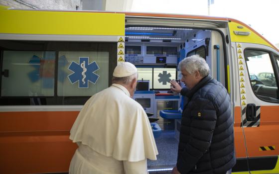 Pope Francis stands outside an ambulance with an older white man in a puffy jacket