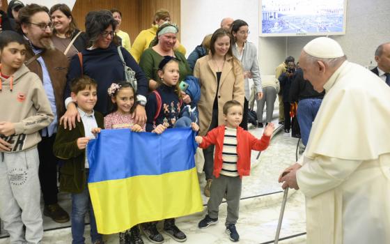 Pope Francis, using a cane, speaks with a group of children holding a Ukrainian flag and their adults
