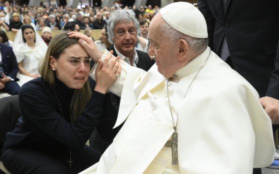 Pope Francis places his hand on the head of a woman who cries with emotion
