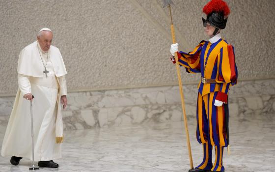 Pope Francis uses his cane to walk by a member of the Swiss Guard, who wears brightly colored stripes