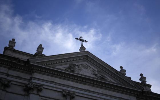 A view of the shadowed upper half of a stone church topped by a cross and the sky