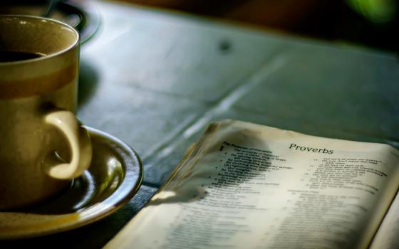 The Bible open to the Book of Proverbs, sitting next to a coffee cup (Unsplash/Alex Shute)