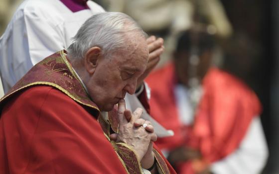 Pope Francis, dressed in red and gold and without a zucchetto, bends his head in prayer