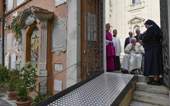 Pope Francis prays, sitting in a wheelchair at the top of a ramp down to a courtyard
