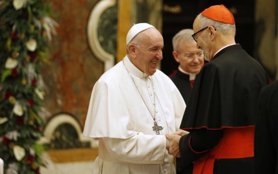 Pope Francis shakes hands with an older white cardinal. Another man is in the background