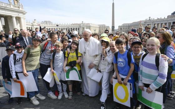 Pope Francis stands among a group of children who look elementary-school-aged in St. Peter's Square