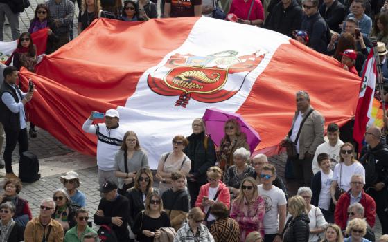 A crowd stands in St. Peter's Square, with a group holding a very large red and white Peruvian flag