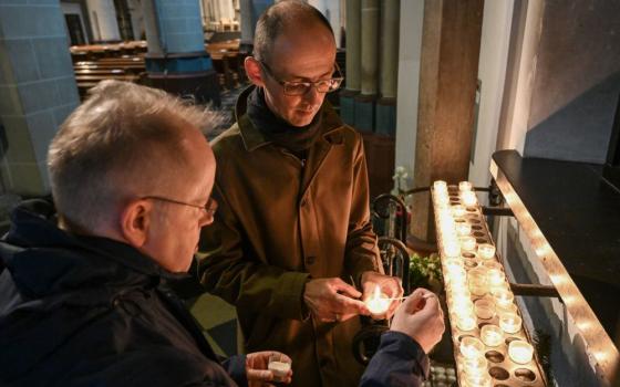Two men light votive candles in a church.