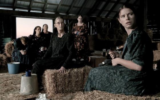 A still shot of the movie "Women Talking" shows women sitting in a barn.