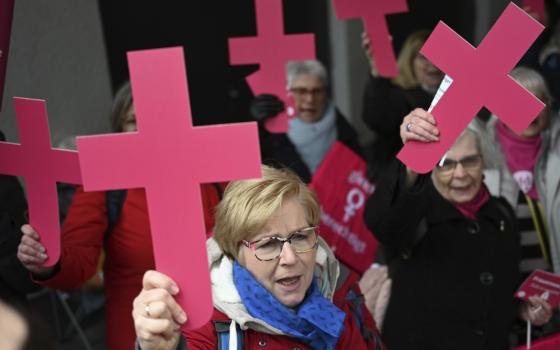 Women, wearing winter coats, energetically hold pink crosses above their heads