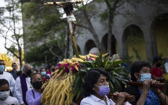 Three masked women can be seen carrying a crucifix on their shoulders surrounded by a larger masked crowd