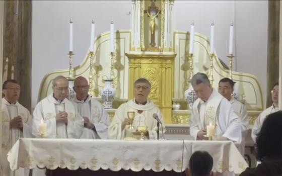 A group of priests wearing white vestments stands behind an altar covered in a white cloth