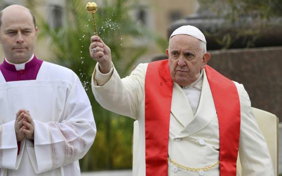 Dressed in a white coat and a red stole, Pope Francis holds aloft a holy water sprinkler