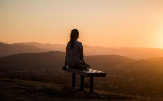 Woman sitting on bench looking out over mountain range (Unsplash/Sage Freidman)
