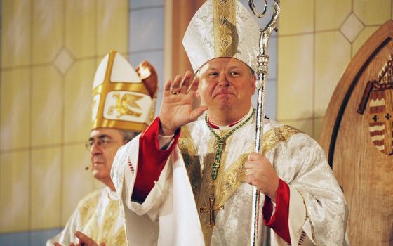 Bishop Richard Stika waves to the congregation during his episcopal ordination March 19, 2009, at the Knoxville, Tennessee, convention center. Stika, a St. Louis native, is the third bishop to lead the Diocese of Knoxville, which was founded in 1988 and is home to almost 60,000 Catholics.. At left is Cardinal Justin Rigali of Philadelphia. (CNS/East Tennessee Catholic/Deacon Patrick Murphy-Racey,)