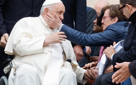 A person touches Pope Francis' cheek as he rides in his wheelchair past a line of people 