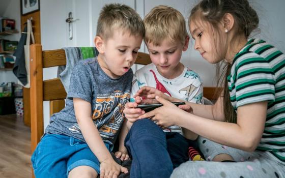 Stanislav Tereshchenko, 5, Janek Sulkowski, 8, and Anastasia Tereshchenko, 9, play Minecraft on a portable tablet at the home of Olga and Mariusz Sulkowski in Otwock, Poland, May 21, 2022. (CNS photo/Lisa Johnston)