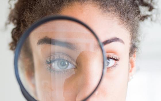 A woman looks through the lens of a magnifying glass (Dreamstime/Aaron Amat)