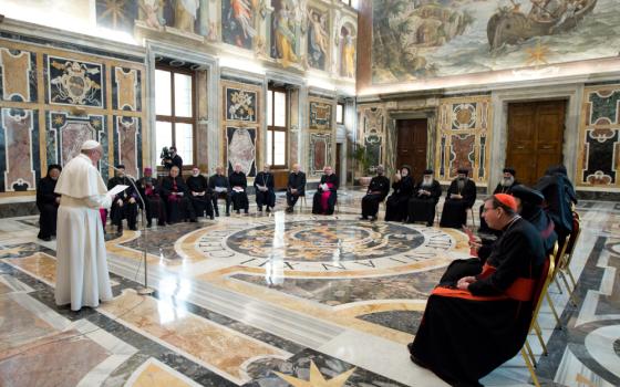 Pope Francis stands up and addresses a group of leaders in Roman Catholic and Orthodox garb in a room with Baroque art