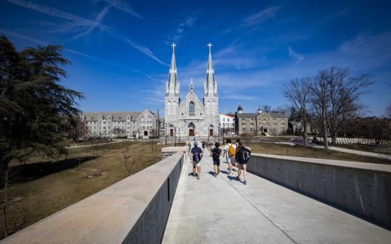 Young adults with backpacks walk down a sidewalk towards a church with two spires