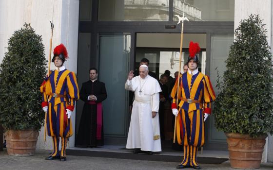 Pope Francis walks out of glass doors between members of the Swiss Guard