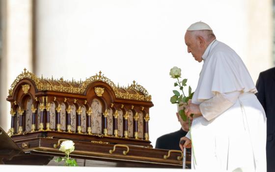 Pope Francis carries a white rose towards an ornate gold and wooden box