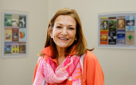 A woman with light brown hair and wearing a pink and orange scarf and orange shirt smiles into the camera