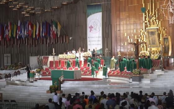 Many priests in green vestments surround a green altar. Many flags are on the wall next to the altar.