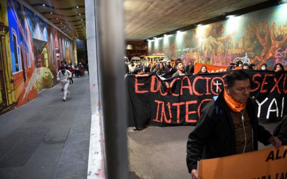 Bolivian people march under a roofed passage holding large black and orange banners