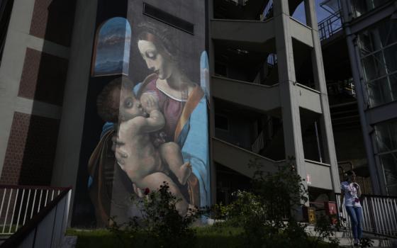 A large banner painting of a white woman breastfeeding a white baby hangs on the side of a building