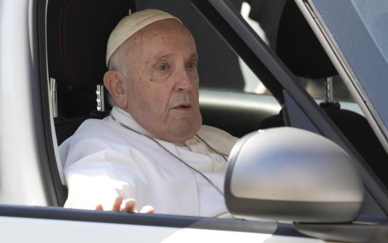 Pope Francis sits in a car with his hand on the door and his mouth slightly open