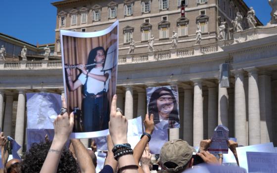 People hold up pictures of a black-haired girl, including one where she is playing the flute, while standing in St. Peter's Square below Pope Francis' open window